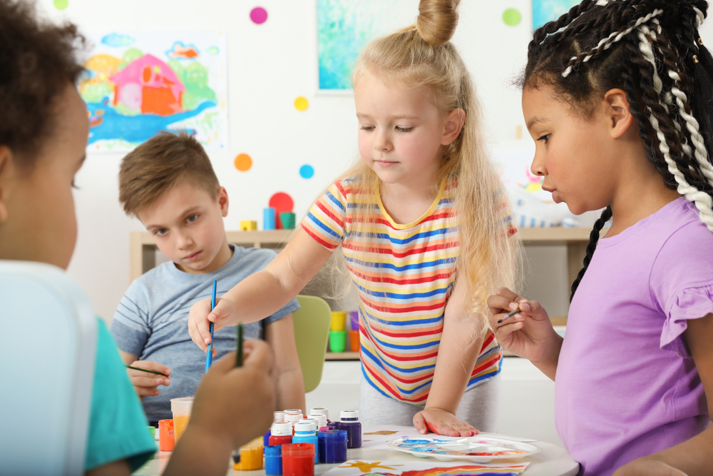Crianças realizando atividades bilíngues com pintura e interação em sala de aula.