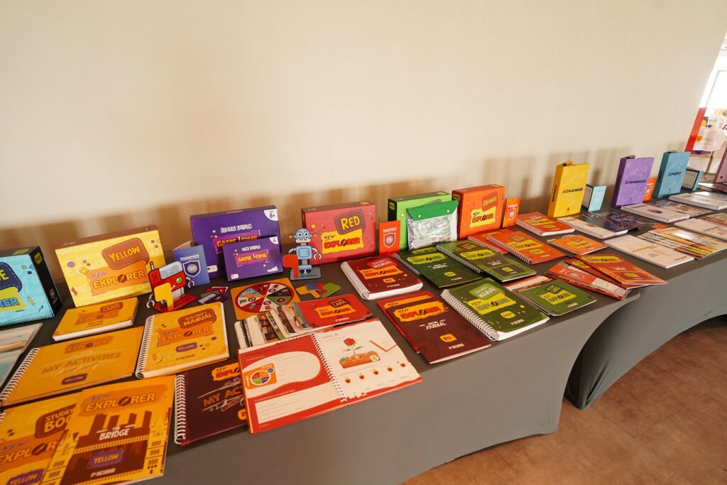 Exposição do material didático da International School, com diversos livros, cadernos e recursos educacionais organizados.