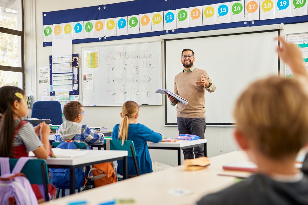 Professor ensina alfabeto em sala de aula para crianças do Ensino Fundamental, em ambiente escolar colorido e interativo.