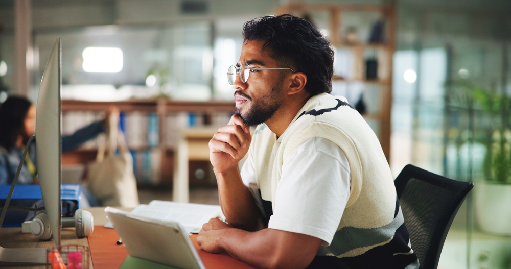 Homem estuda com computador e livros, representando diferentes formas de aprendizagem com uso de tecnologia.