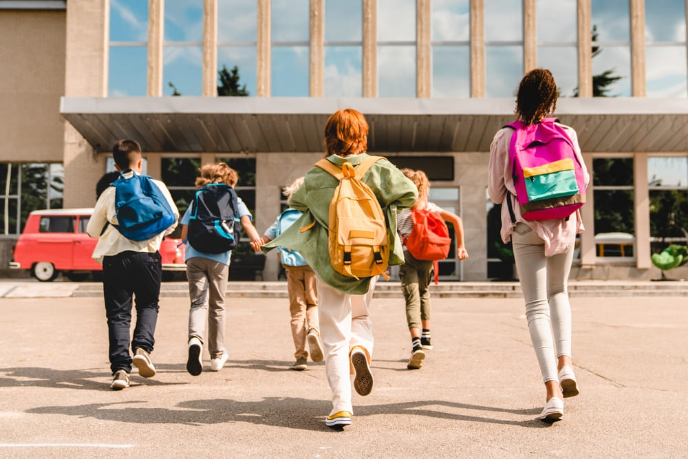 Crianças chegando à escola com mochilas, simbolizando aumento de matrículas após estratégias de captação de alunos.