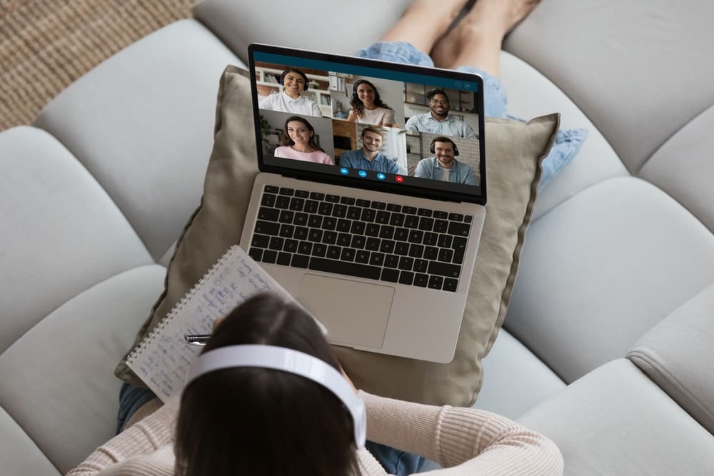 Pessoa participando de videoconferência em aula remota, anotando em um caderno.