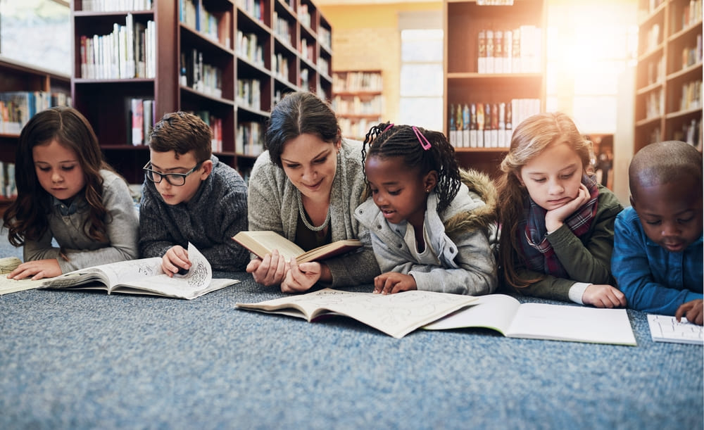 Crianças e professora lendo livros em inglês na biblioteca, ambiente educacional tranquilo.