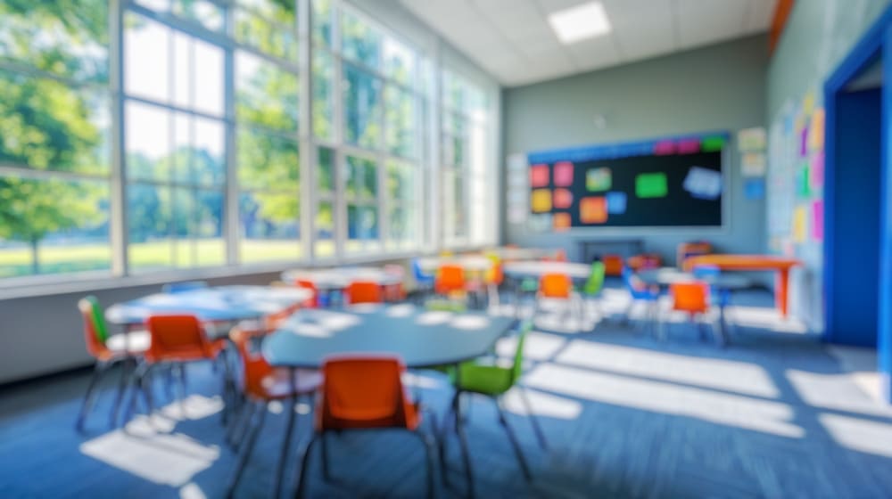 Sala de aula moderna com mesas circulares, cadeiras coloridas e luz natural.