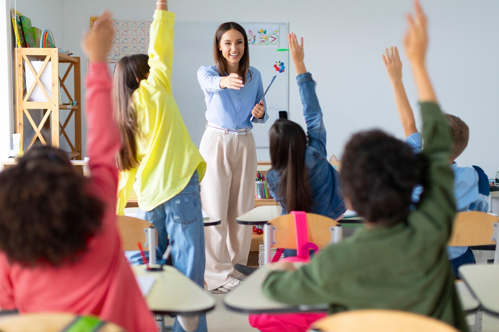 Alunos levantando as mãos em sala de aula multicultural durante dinâmica pedagógica interativa