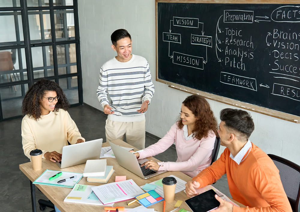 Professores na escola em reunião colaborativa, discutindo estratégias de ensino e trabalho em equipe em frente a uma lousa.