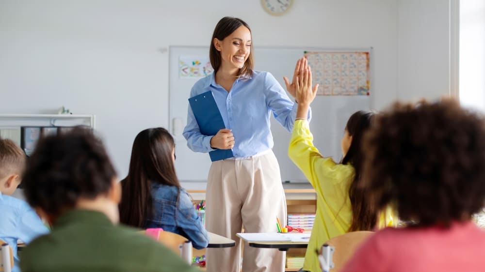 Professora sorridente cumprimenta aluno em sala de aula, representando o corpo docente escolar.