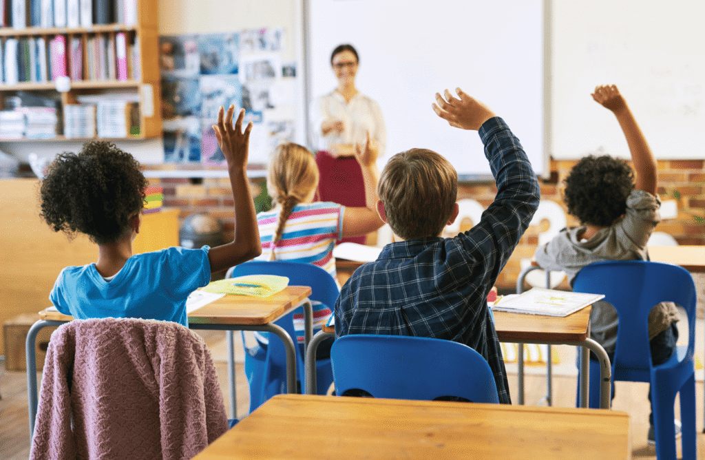 Crianças levantando a mão em sala de aula para responder, seguindo as regras na sala de aula de respeito e participação.