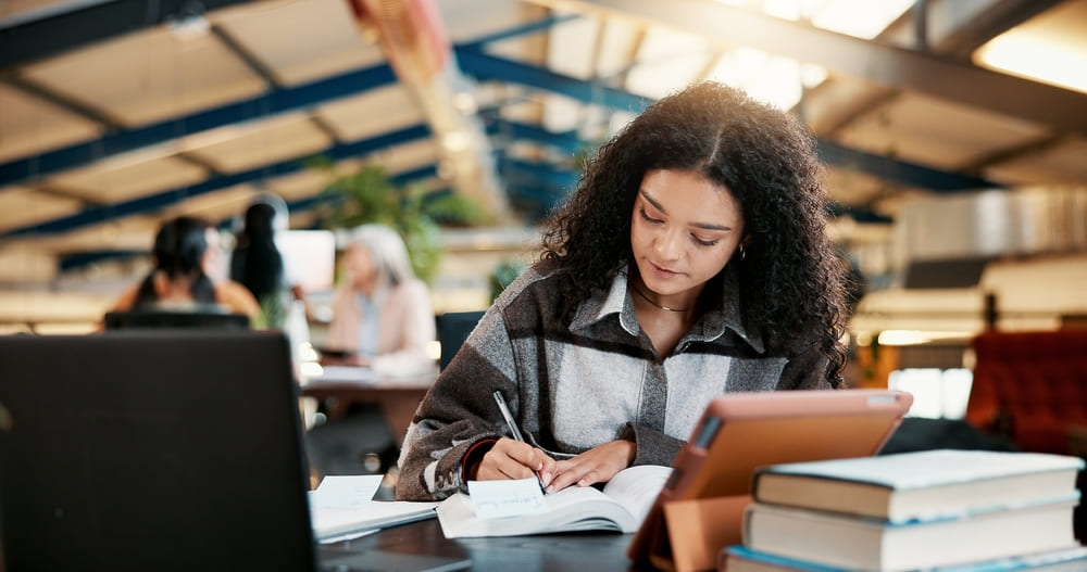 Estudante aplicando métodos de estudo, escrevendo em um caderno e organizando seus materiais em uma mesa de estudo.