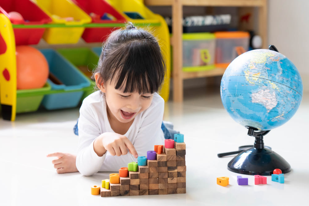 Criança brincando com blocos coloridos e globo terrestre, estimulando o desenvolvimento infantil.