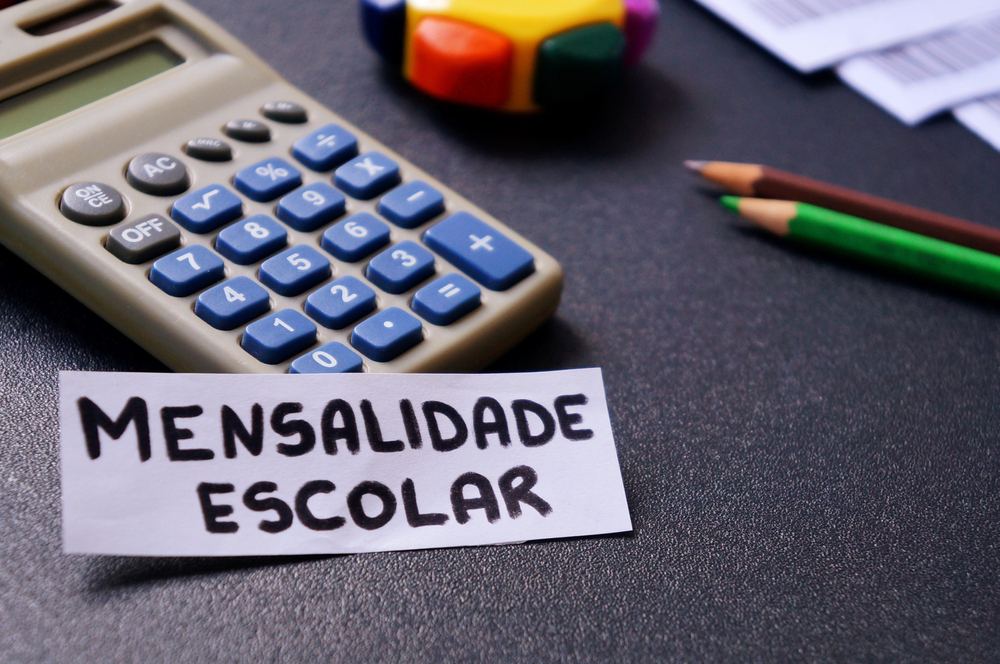 Planejamento financeiro envolvendo mensalidade escolar com calculadora e notas de real.